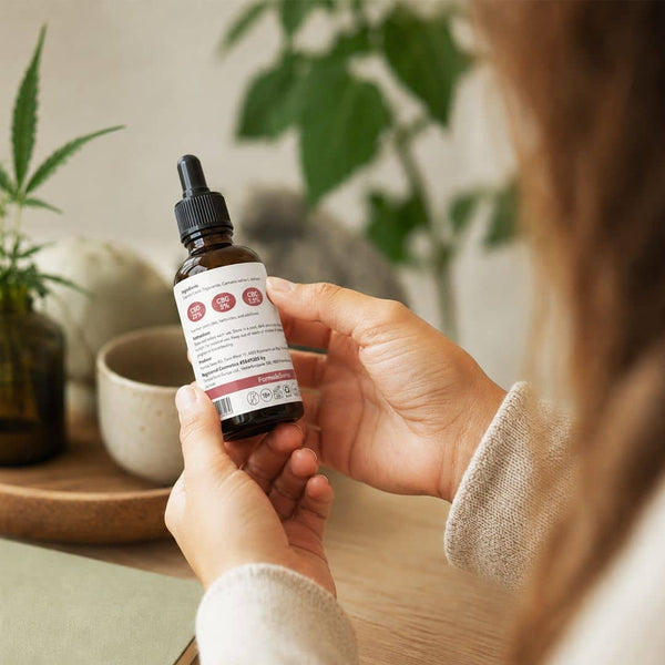 Woman reviewing the label on a Formula Swiss cannabinoid oil bottle in a bright indoor setting.